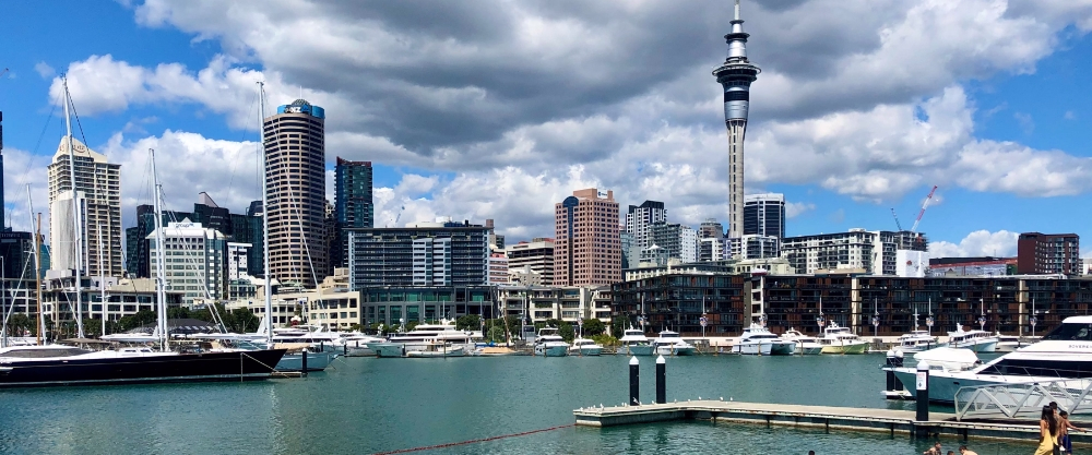View of Auckland Harbour with yachts and boats moored in turquoise waters, highlighting the city skyline with modern skyscrapers and the iconic Sky Tower.